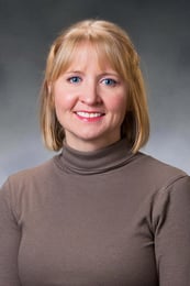 Amber smiling in front of a gray background with a brown turtleneck.