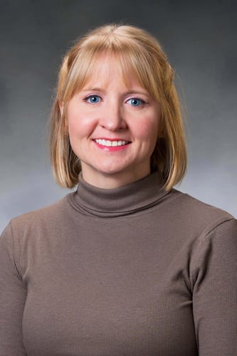 Amber smiling in front of a gray background with a brown turtleneck.