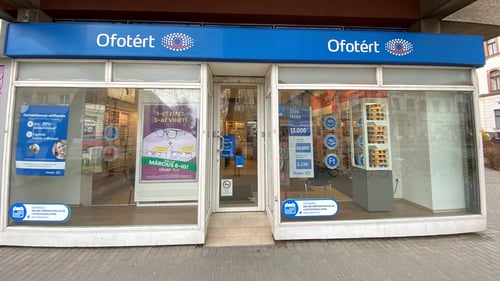 Ofotért üzlet bejárata Kiskunfélegyházán, a Kazinczy utcában, üvegportállal és kirakati plakátokkal.