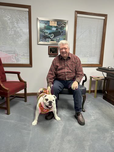 Agent Bill with his dog Bentley sitting in a chair on a blue carpet.