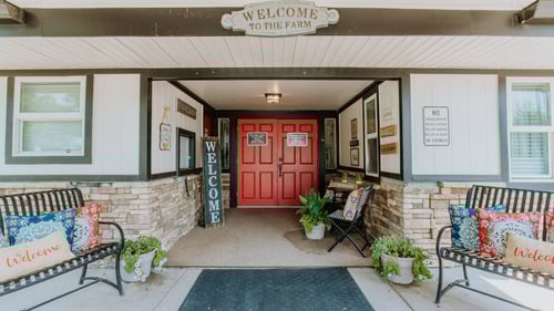 Inviting front entrance with red double doors, welcome signs, benches, and potted plants at Foxridge Farm Business in Aurora, CO