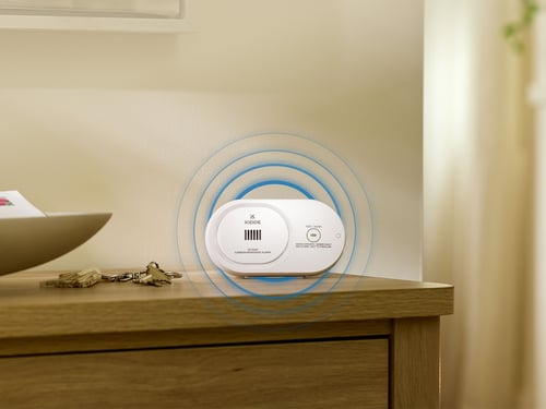 A CO alarm sitting on a table, with circles showing sound emanating from the device.