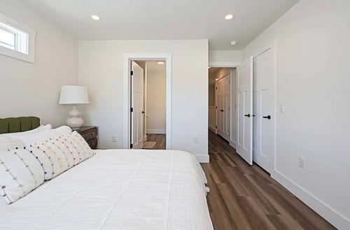 Modern rental home bedroom featuring wood-plank flooring, white interior doors, and a bed with a textured white comforter.