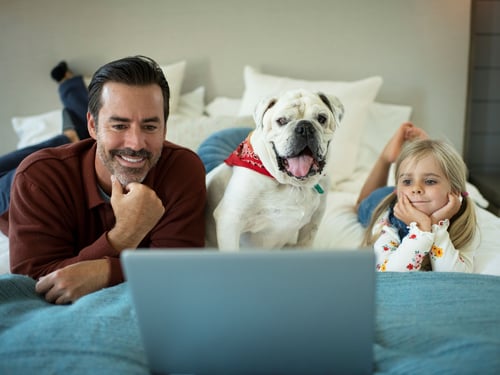 Dad with daughter and family dog streaming a movie on their laptop on bed
