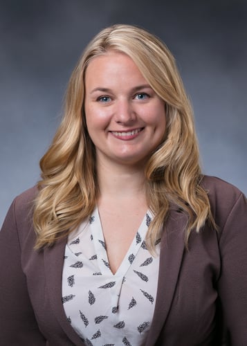 Tianna Seeley, APRN, CNP smiles in front of a gray background .