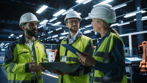 Three workers with tablet and laptop in manufacturing plant