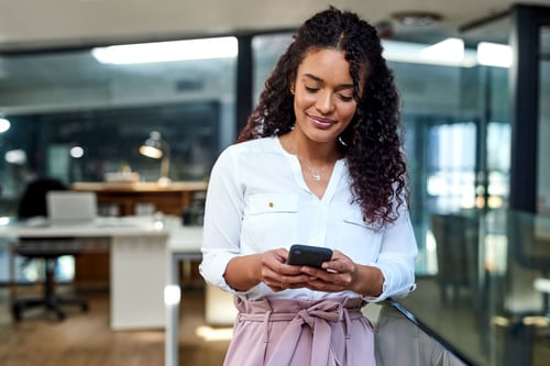 Woman standing in office looking down at phone