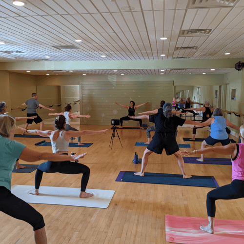 Participants engaged in a group yoga class at Cornerstone Health & Fitness, stretching and holding poses. The instructor leads the group with clear guidance in a well-lit studio, showing the community aspect of wellness in the best gym near you.