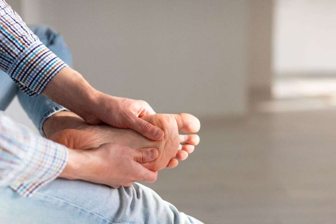 Man with morning foot pain holding the bottom of his foot
