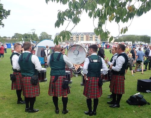 pipe band standing in a circle in a field, practicing in front of a manor house