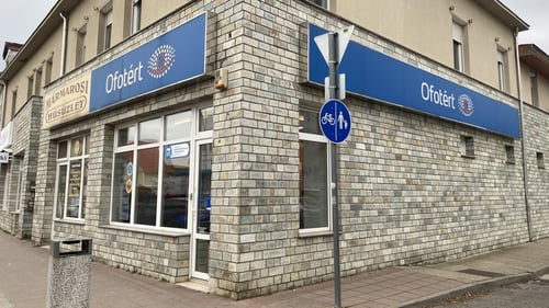 Ofotért üzlet homlokzata Pakson, a Dózsa György úton, saroképület kék cégtáblával és üvegportálokkal.