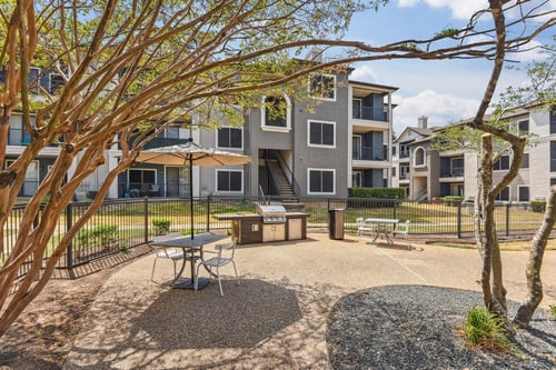 A courtyard with a picnic table surrounded by trees and apartment buildings at Onyx183 in Austin, TX