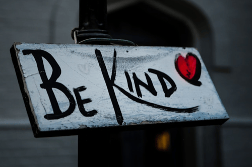 A white wooden sign attached to a lamp post that says "Be kind."