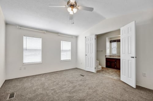a bedroom with a ceiling fan and a bathroom in the background
