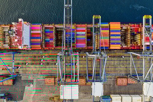 An aerial view of a cargo ship and dockside logistics operations.
