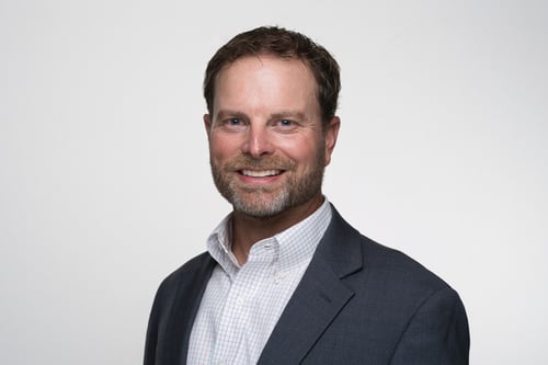 Agent Aaron Loetscher standing and smiling wearing white button up shirt with black suit blazer