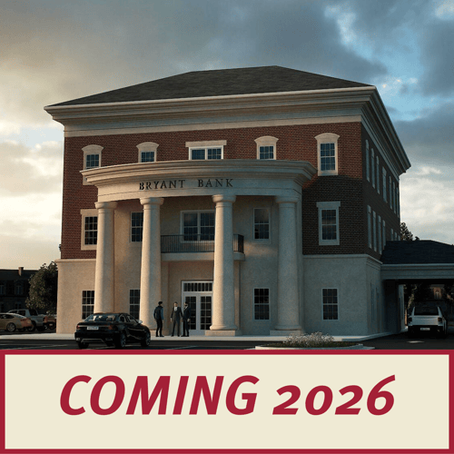 An architectural rendering of a grand, three-story brick Bryant Bank building with a neoclassical white columned entrance. A red banner across the bottom reads "COMING 2026" in bold cream lettering.