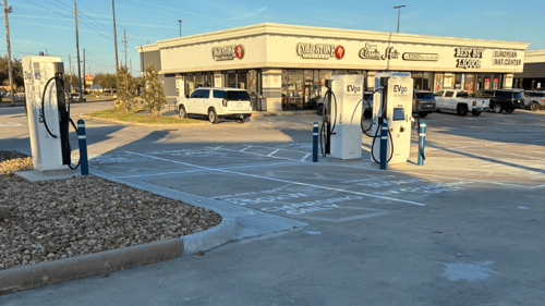Several EVgo fast-charging units installed in marked parking spaces at a public charging station, with EVgo logos on the chargers, protective bollards around each unit