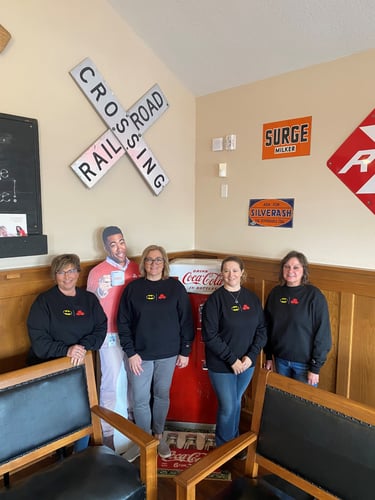 Agent Toni Nadeau and three female team members standing indoors with black long sleeve t-shirts on and two chairs in front of them