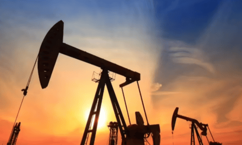 Oil pump jacks silhouetted against an orange and golden sunset sky