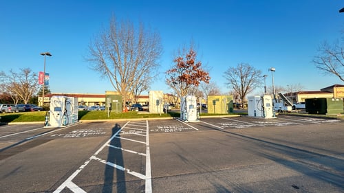 Several EVgo fast-charging units installed in marked parking spaces at a public charging station, with EVgo logos on the chargers, protective bollards around each unit