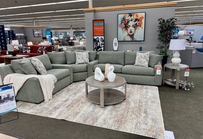 Soft sage green sectional sofa with modern art and round wood tables on display at Slumberland Furniture Burlington in Burlington, Iowa. Shop contemporary sectionals and living room furniture locally.