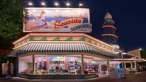 A kiosk beneath a lighthouse-like tower and a huge billboard sign with an illustration of a crab, a bucket of seashells, a beach, an ocean pier and the words "Seaside Souvenirs."