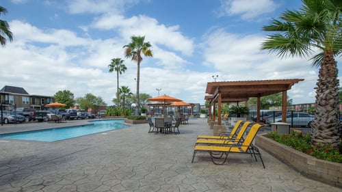 A pool area with a patio, chairs and umbrellas at Willow Creek Apartments, Texas