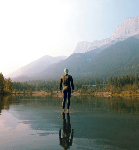 Un homme debout dans un lac avec des montagnes en arrière-plan.