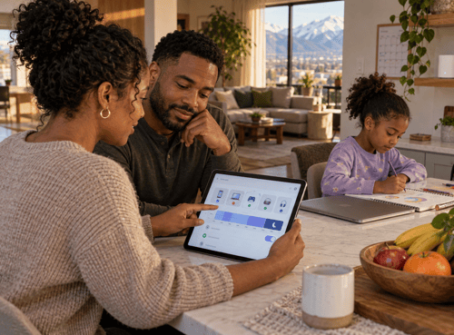 Parents review Wi-Fi parental controls on a tablet at the kitchen island while their daughter draws beside a closed laptop.