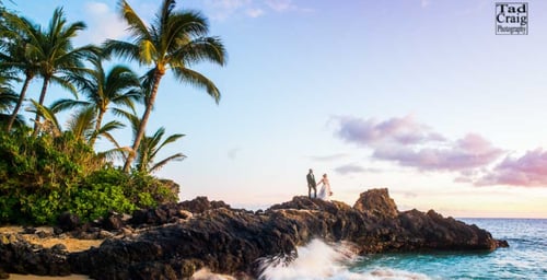 married couple standing on rocks next to the ocean