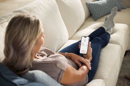 Woman lounging, looking at a notification from her Kidde App on her phone.