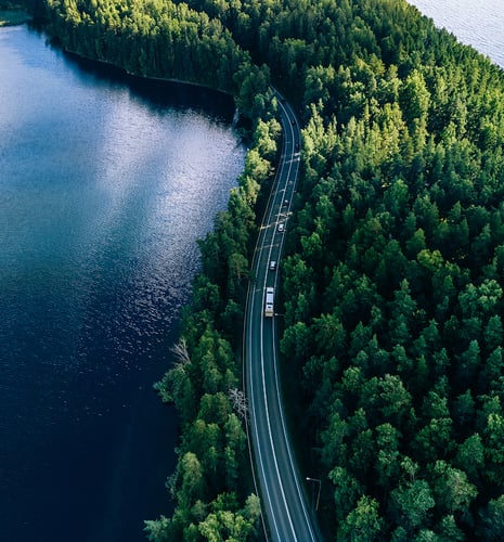 An aerial shot of a winding road on a lush green peninsula surrounded by deep blue water.