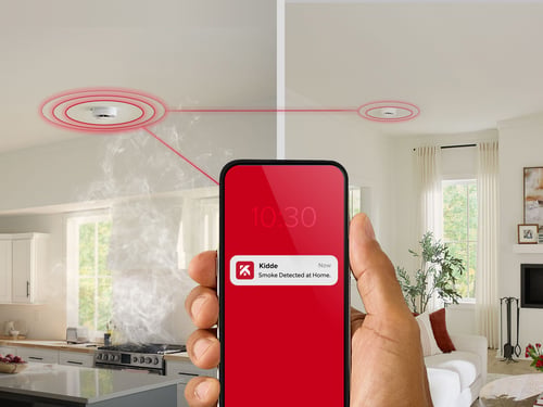 Two alarms sounding in the background, with red circles showing the sound eminating, and a smart phone with a notification from the Kidde app in the foreground, connected to the alarms going off.
