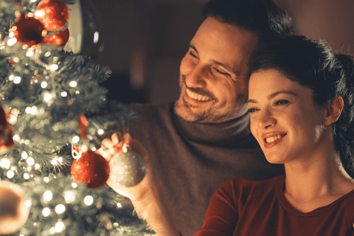 Couple hanging up a Christmas tree ornament.