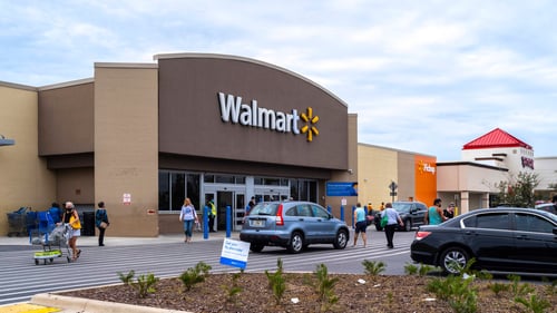 People sporadically around parking lot of Walmart with blue hatchback in front