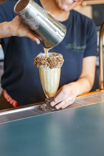 Bartender pouring boozy milkshake into a glass with cookie crumbles