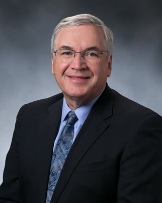 Dr. Will Hurley smiling in front of a gray background.