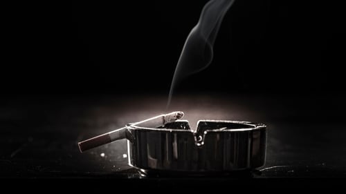 A close-up shot of a cigarette resting on an ashtray, with a delicate wisp of smoke rising, highlighting the fire risk associated with smoking.