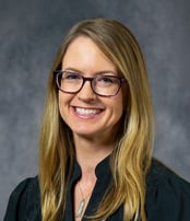 Tammy smiling in front of a gray background wearing a dark green shirt.