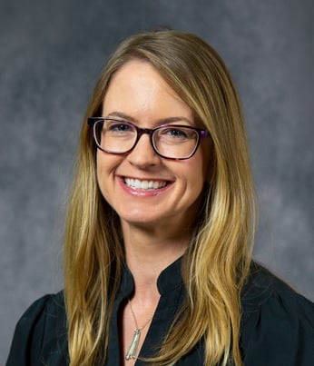 Tammy smiling in front of a gray background wearing a dark green shirt.