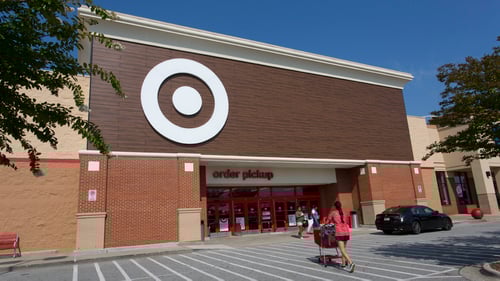 Woman in pink shirt and black shorts pushing shopping cart towards entrance of Target at Wendover Place shopping center