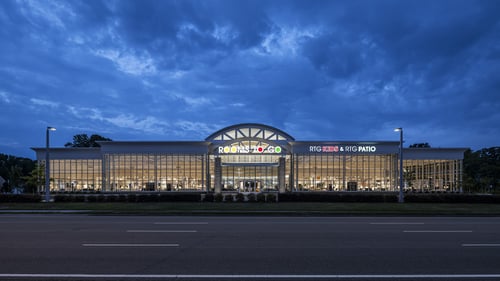 Rooms To Go store facade illuminated at night in Virginia Beach, VA, featuring large glass windows and prominent signage.