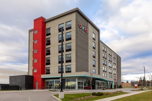 Modern avid hotel exterior with red column and parking lot