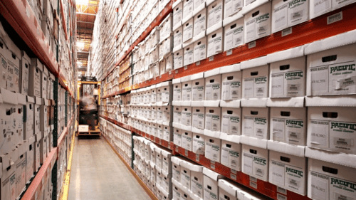 Inside view of Pacific Records Management's records center with boxes stacked floor to ceiling on metal shelving and a forklift in the background