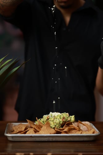 Table-side guacamole and chips with cheese being drizzled on top at El Lugar.
