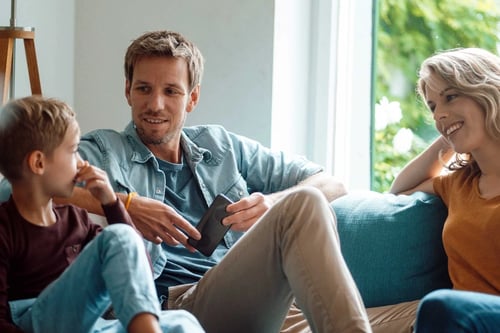 Son talking with mother and father sitting on sofa in living room