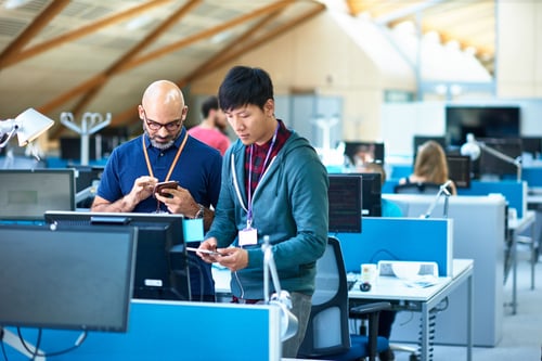 Two men holding phones standing in office space