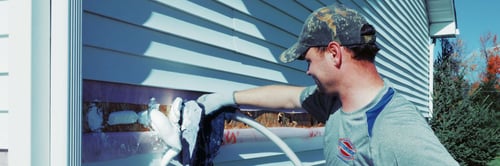 RetroFoam installer insulating a home with vinyl siding.