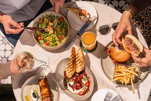 Overhead view of a group of friends sharing a meal of elevated American cuisine, including salads and cocktails, at Matchplay Kitchen in Napa Valley.